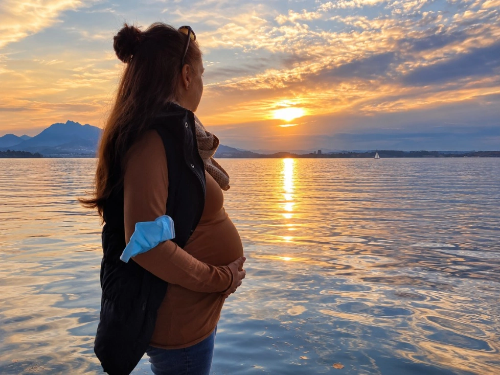Schwangere Frau blickt bei Sonnenuntergang über einen Schweizer See